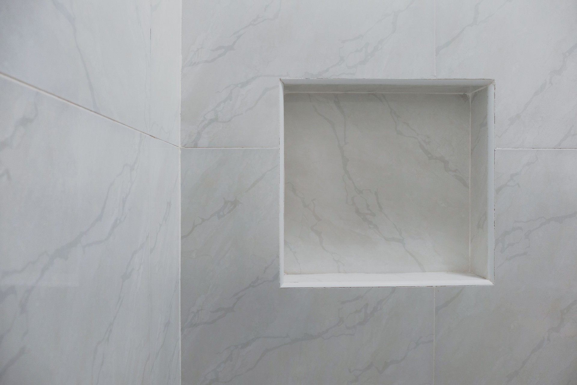 Close up of empty built-in shower caddy in wall recess in bathroom. Modern elegant bathroom interior with marble wall tiles. Display shelf for toiletries logo branding mockup