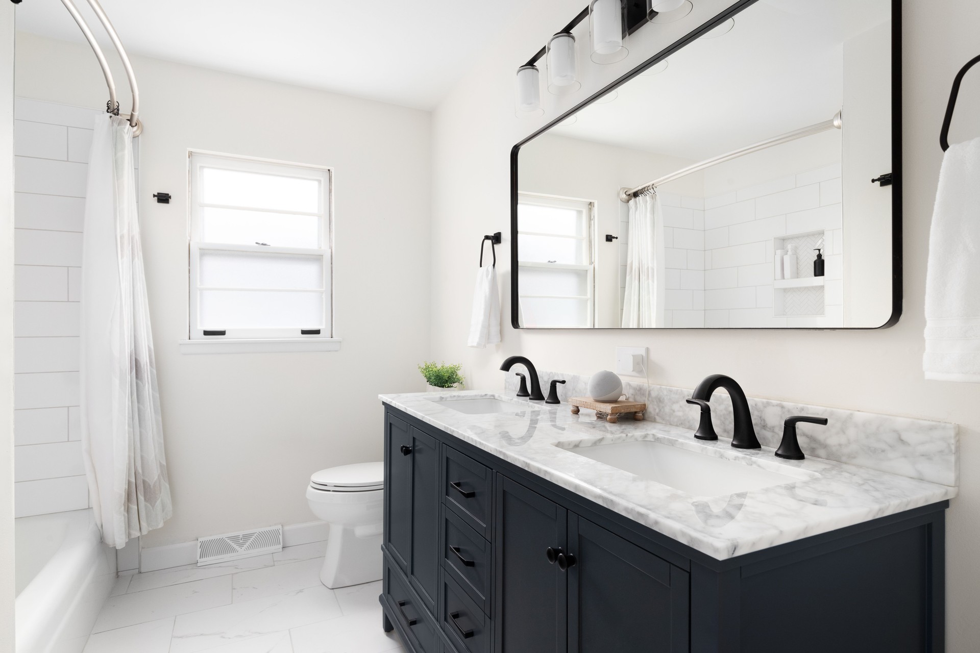 A bathroom with a dark blue cabinet, marble countertop, and subway tile shower.